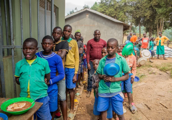 Niños y adultos esperan en fila para la distribución de alimentos al aire libre, lo que refleja el apoyo de la comunidad. Speak Media Uganda.